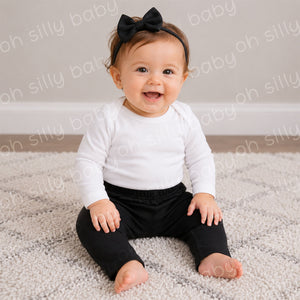 Baby girl wearing black baby cotton pants with a plain white long sleeve bodysuit