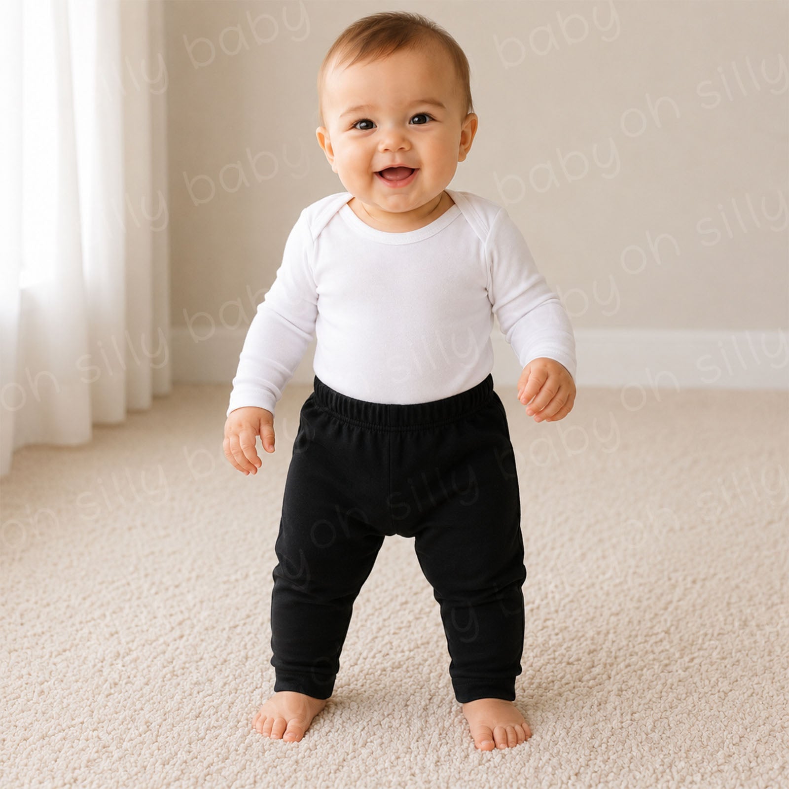 A baby standing while wearing Black Cotton Pants with a white long sleeve baby bodysuit