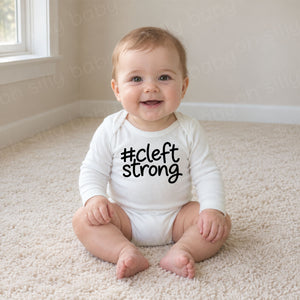 Cleftstrong baby wearing white long sleeve bodysuit with black #cleftstrong design
