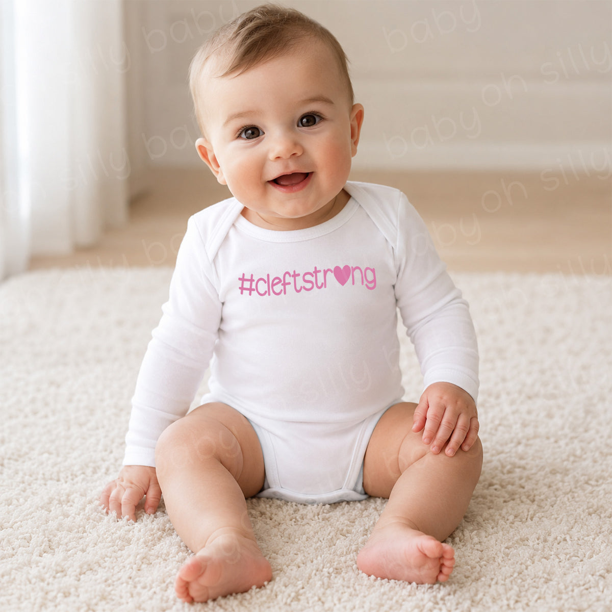 Baby girl wearing a white long sleeve Cleftstrong Heart baby bodysuit featuring a pink Cleftstrong heart design
