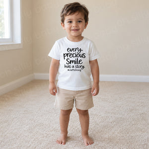 Every Precious Smile Has A Story toddler boy wearing white unisex T-shirt with black #cleftstrong design
