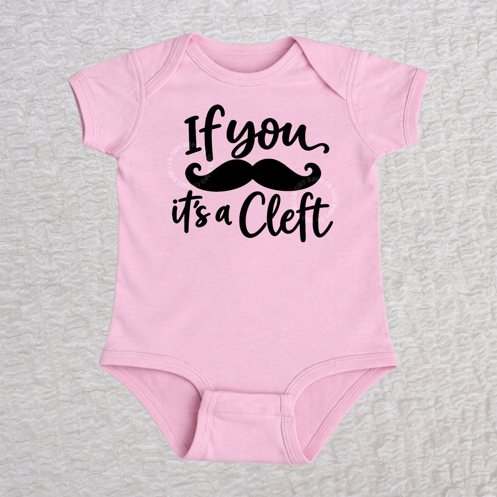 If You Mustache It's A Cleft short sleeve baby bodysuit in pink with black mustache design