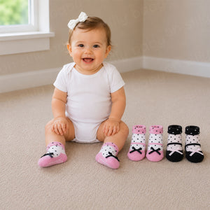 Baby girl wearing pink Olivia Non-Skid Baby Socks with the pink and black sock styles displayed beside her.