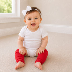 Baby girl wearing red baby leg warmers with a white baby bodysuit while sitting in a neutral nursery