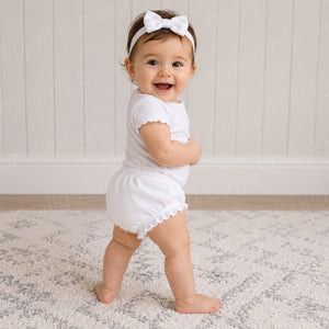 Baby girl wearing a white ruffle diaper cover with a plain white baby bodysuit